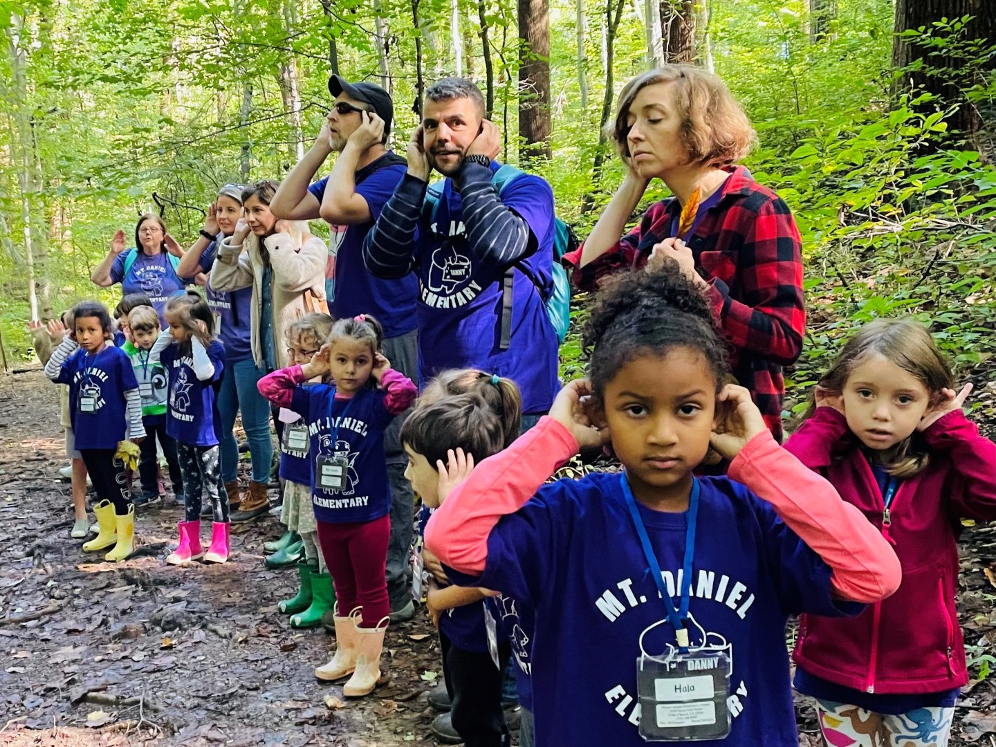 Children and parents outside in the woods with hands cupping ears and listening