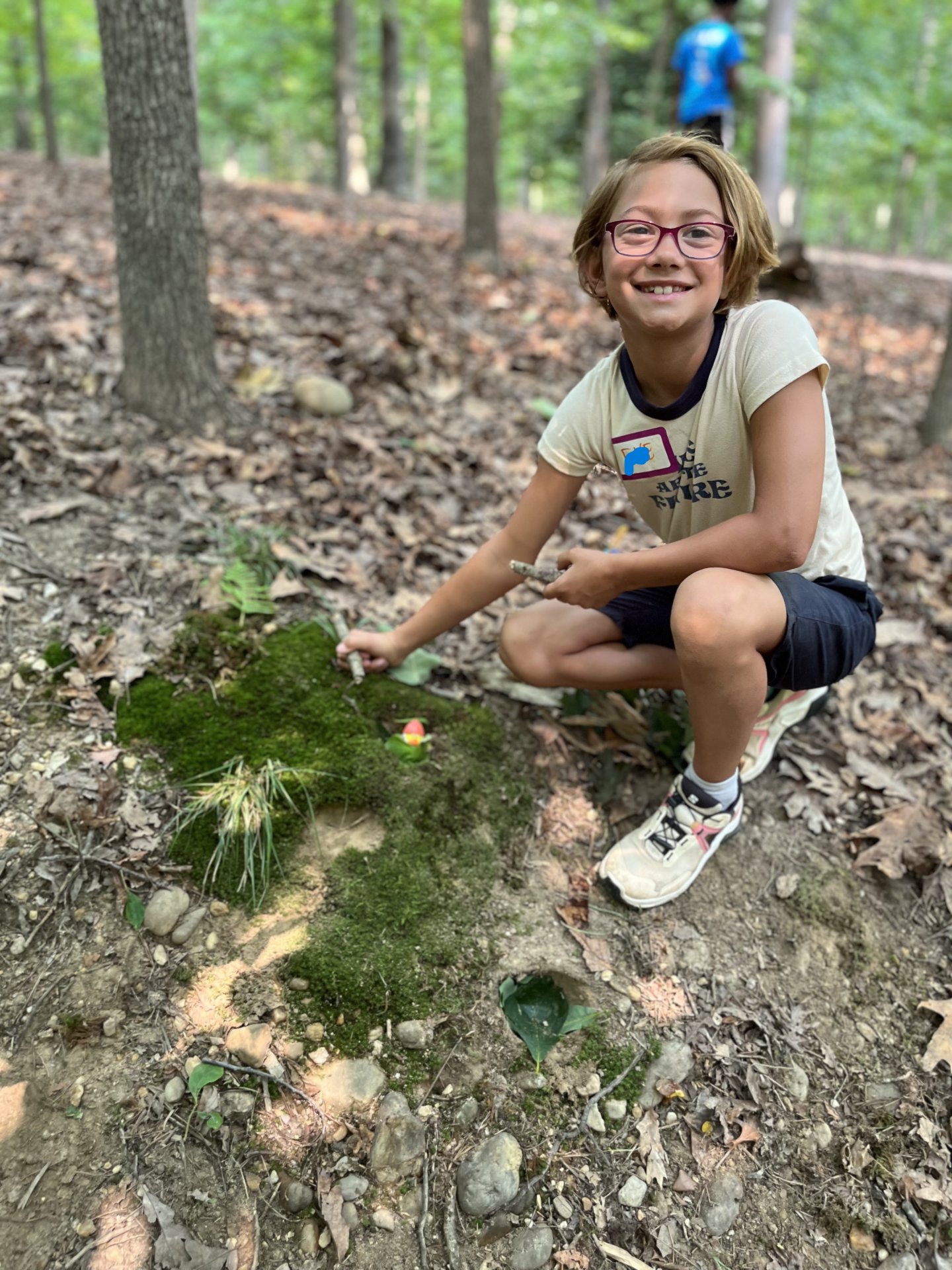 Girl wearing glasses squatting in forest by moss.