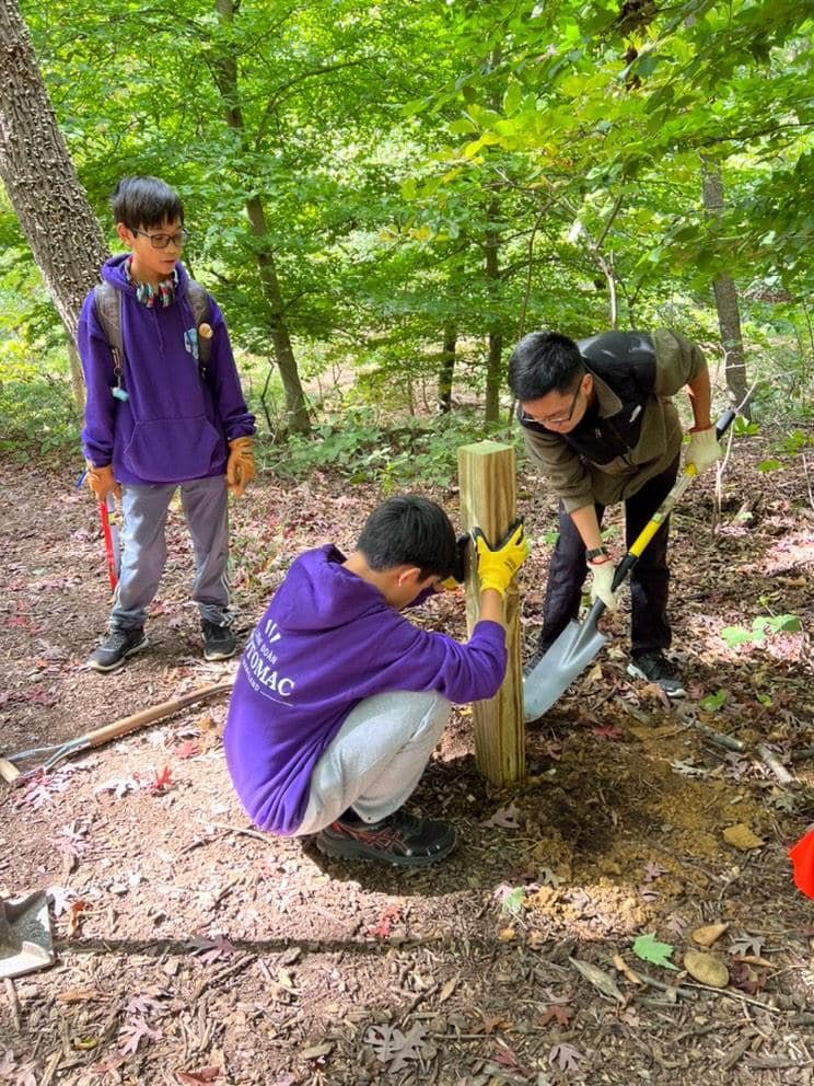 Three teenage boys installing a post at Winkler Botanical Preserve