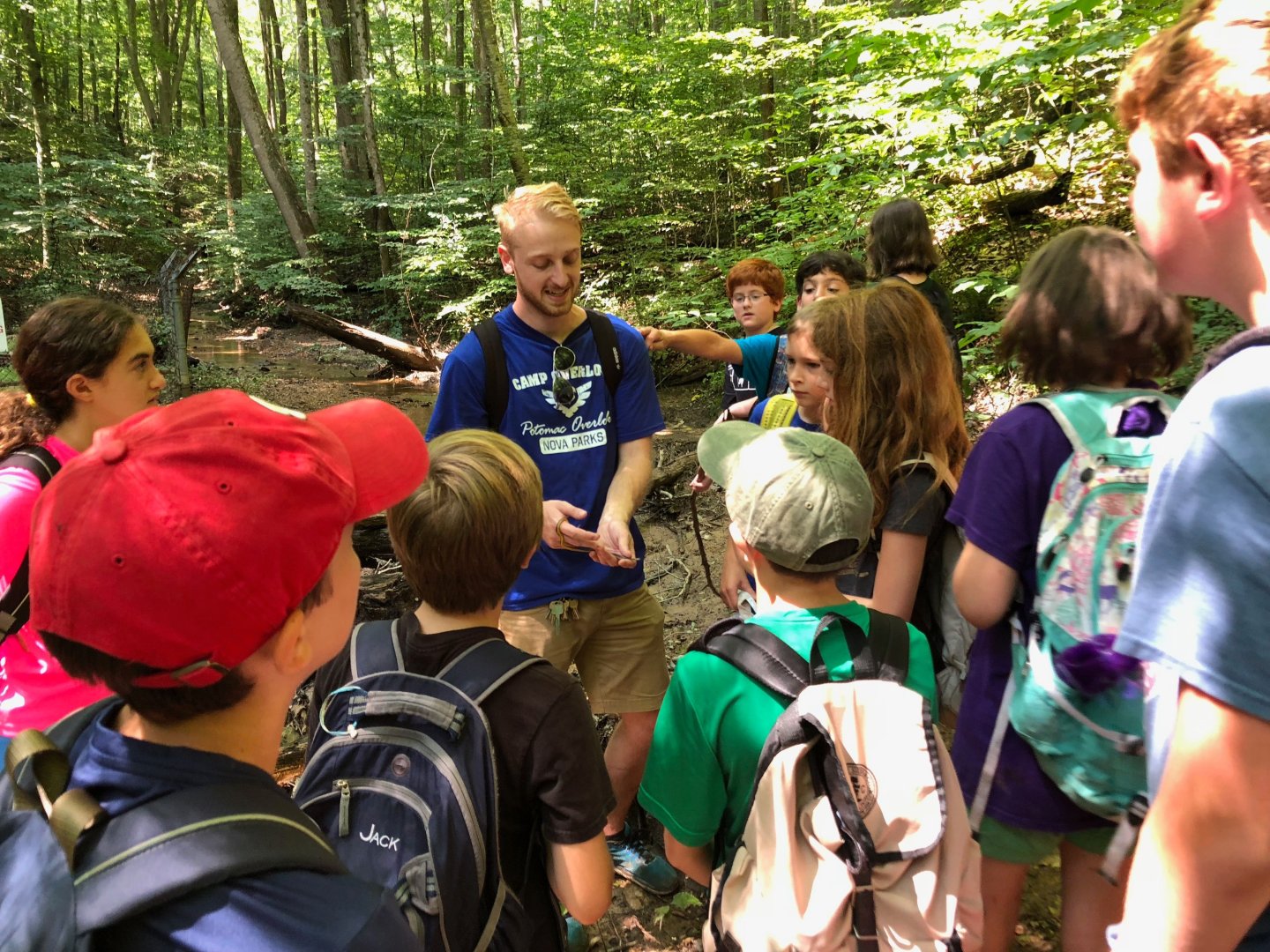 Camp counselor surrounded by campers in the woods on a hike