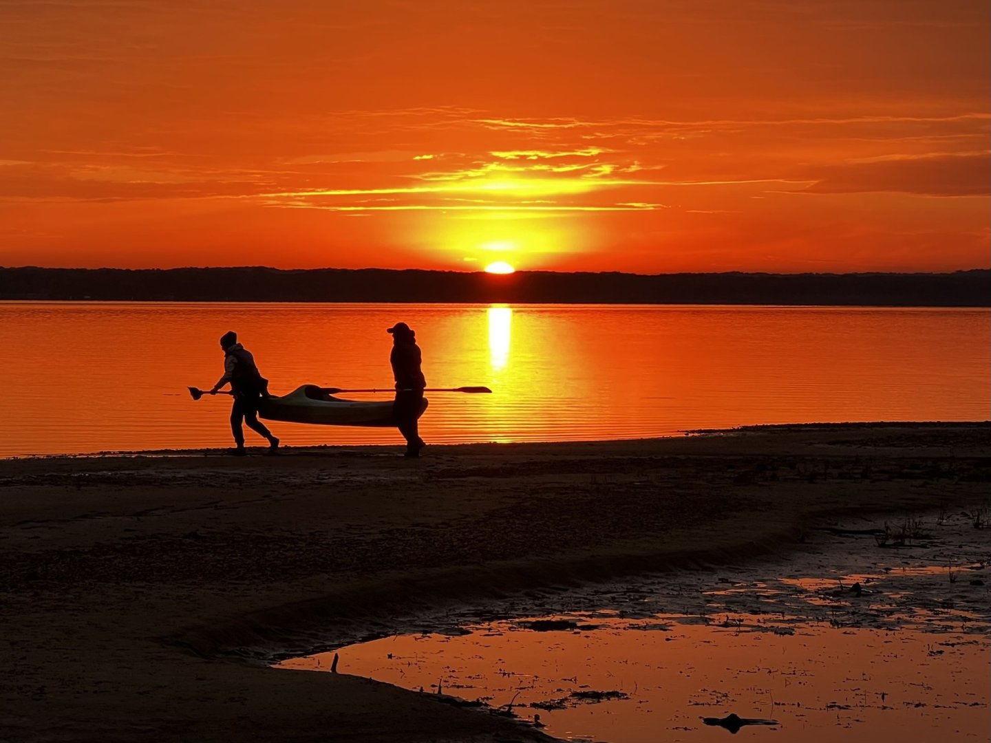 a couple of people walking on the shore at Pohick Bay during a bright orange sunset. the sky is glowing orange