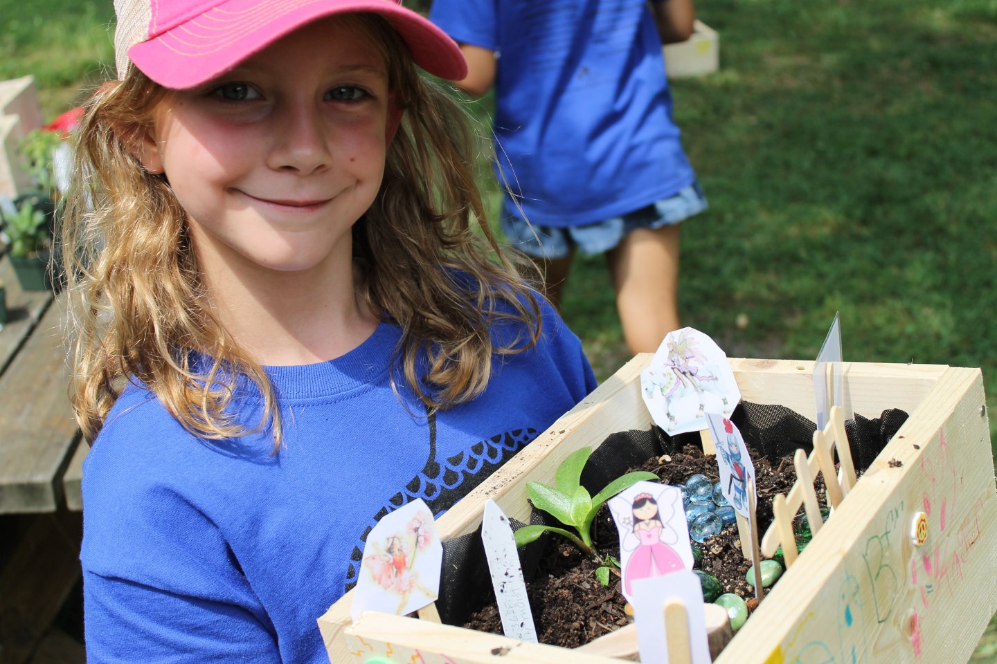 Girl wearing a pink baseball hat smiling and holding her personal garden