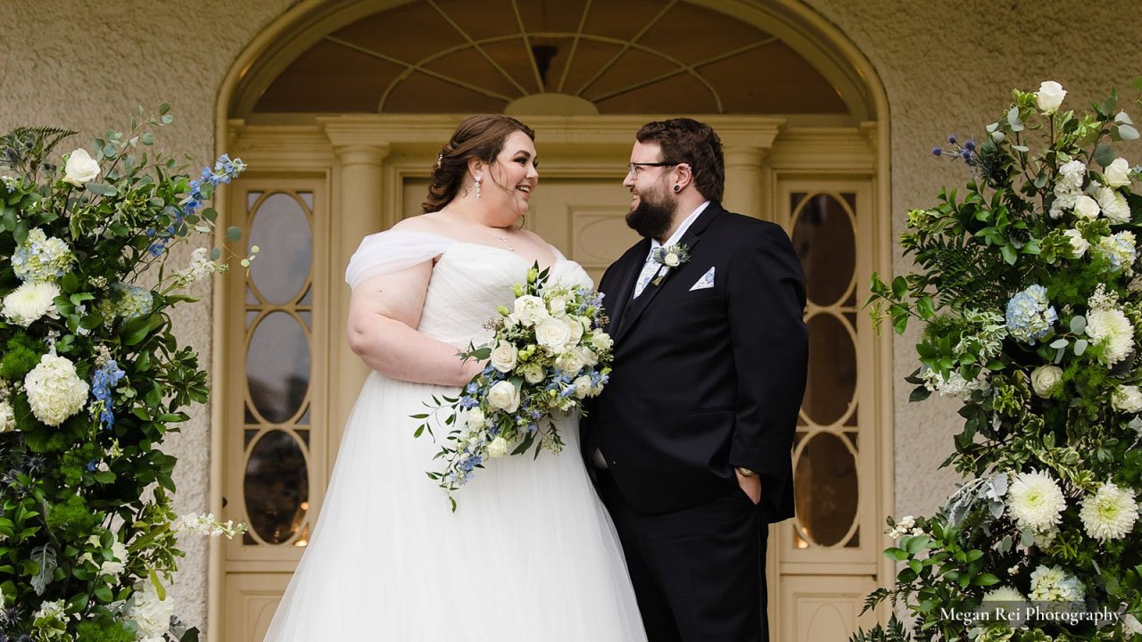 Bride and Groom in front of Rust Manor House front door. Bride is holding a bouquet of white flowers