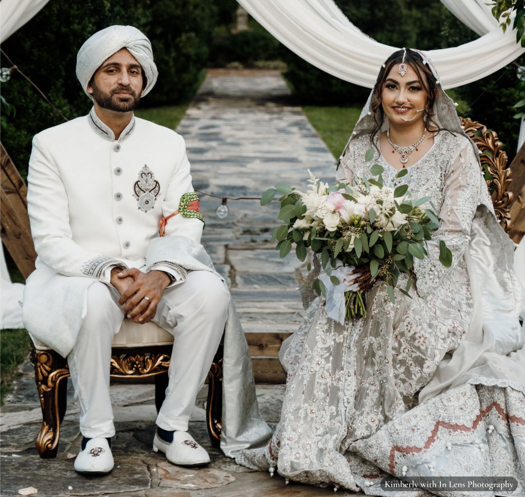 Bride and groom sitting in front of pergola bride holding large bouquet of flowers