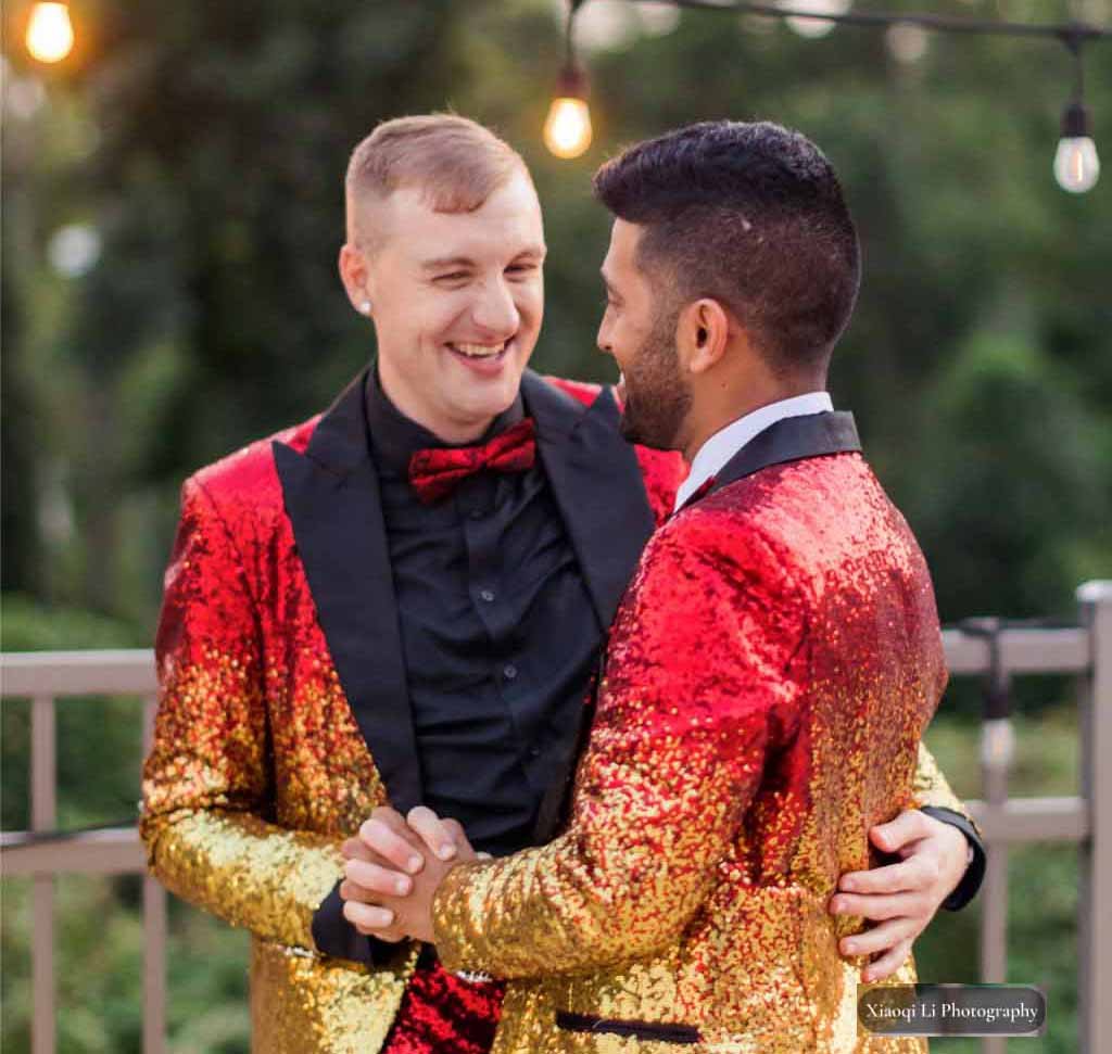 grooms holding hands and smiling at each other. both are wearing red and yellow sequined jackets