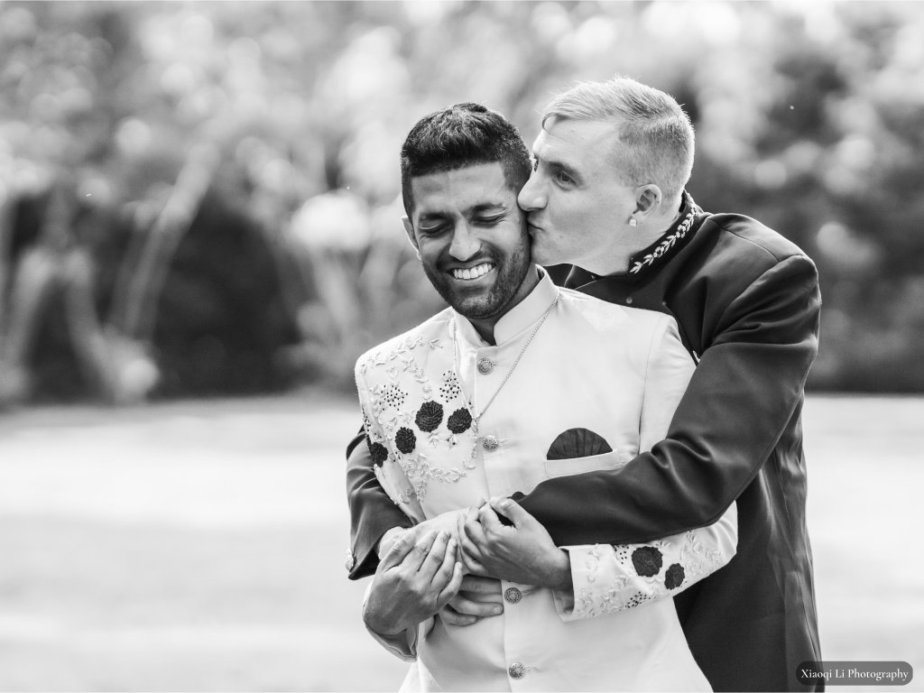 Black and white photo of two grooms hugging and one kissing the others cheek