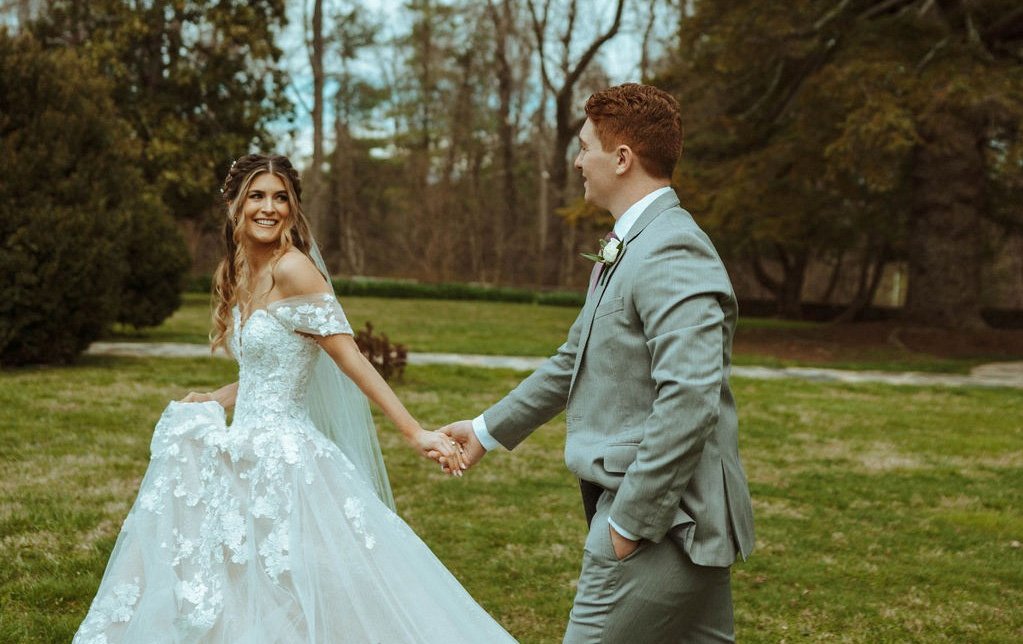 Bride and groom holding hands in the middle of a grass field with blue skies