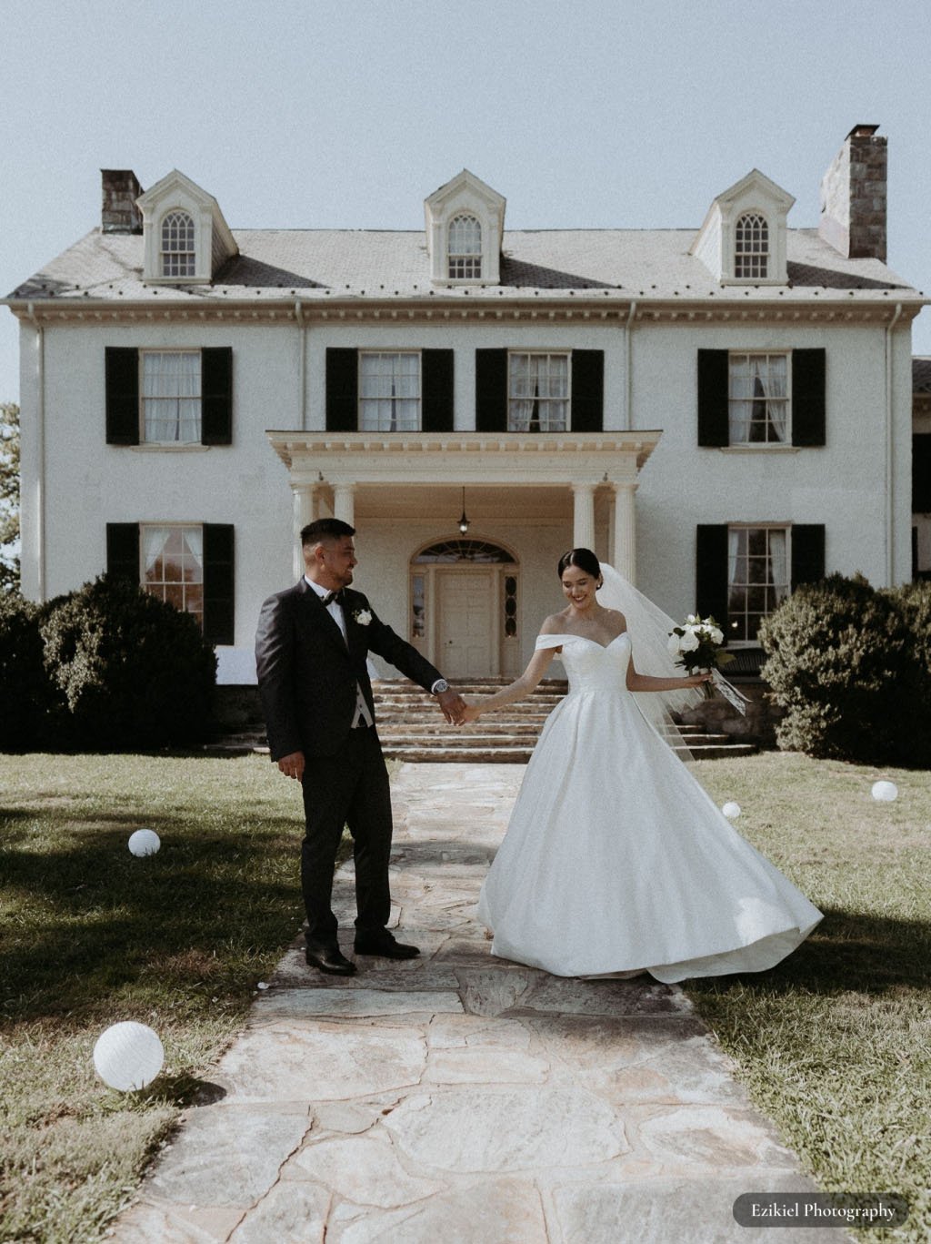 Bride and groom holding hands in front of Rust Manor House white balloons on grass