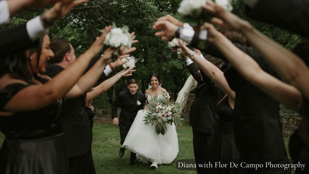 Bride and groom holding hands and running through wedding guests arms in the air