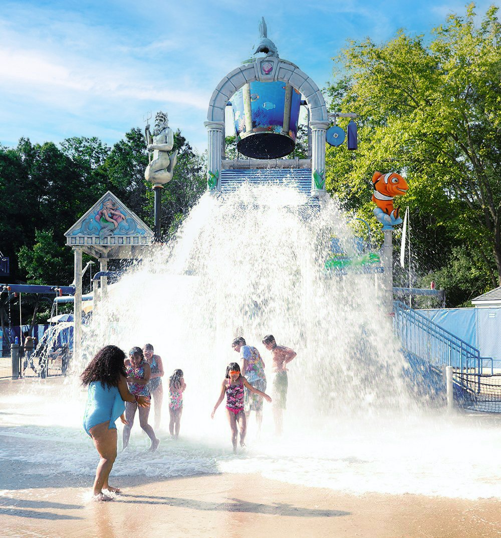 Children playing under a large splash of water at a colorful water park.