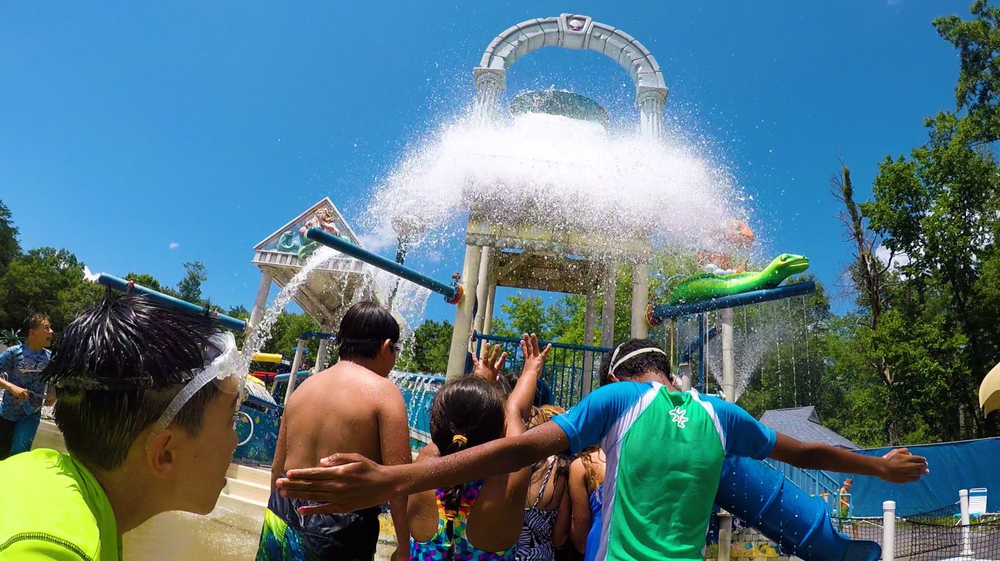 Children playing under a large splash of water at a water park.