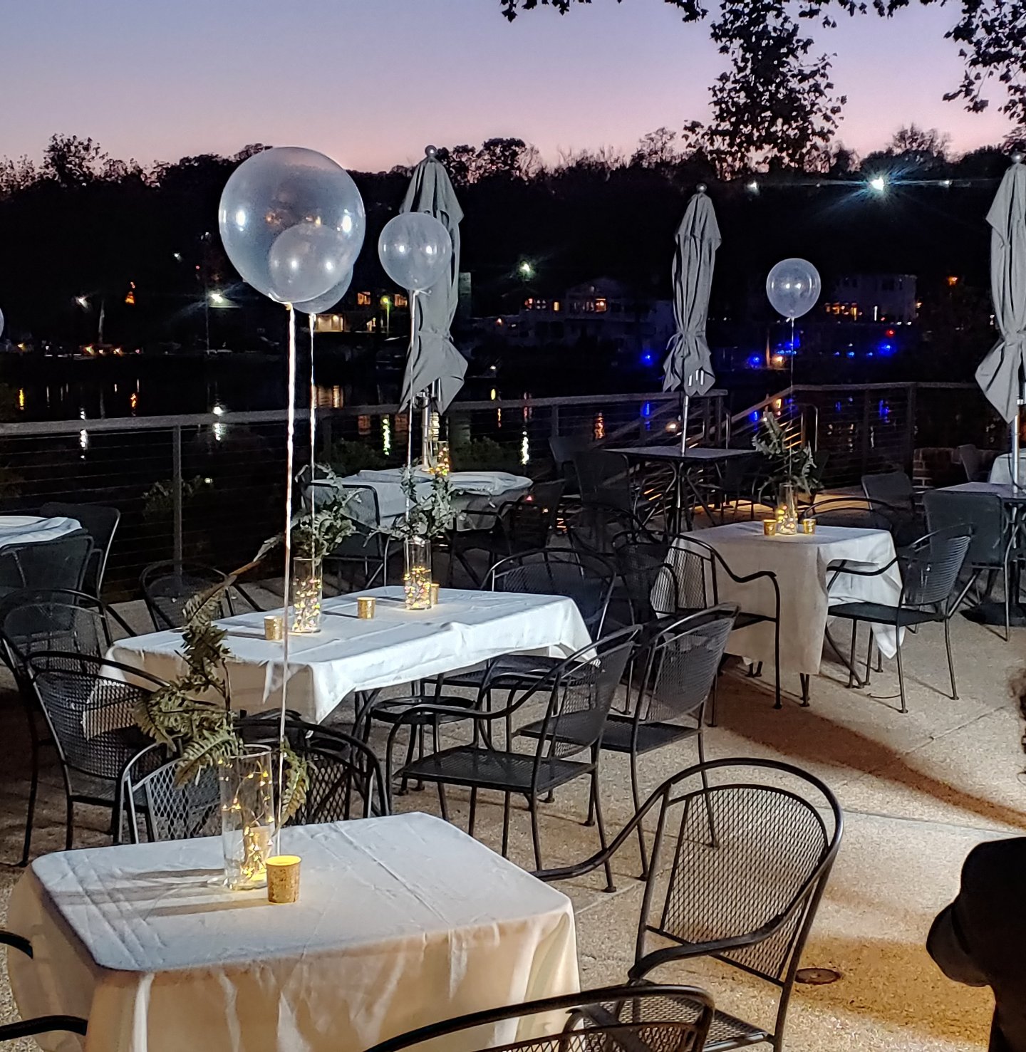 Outdoor restaurant with white tablecloths, balloons, and evening lighting.