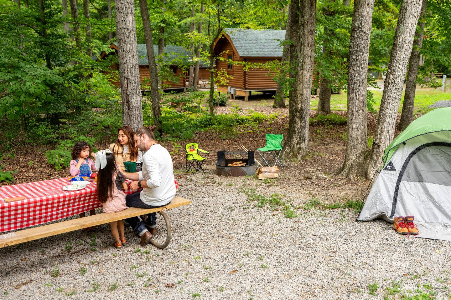 Family enjoying a picnic at a campsite with a tent and cabins in the background.