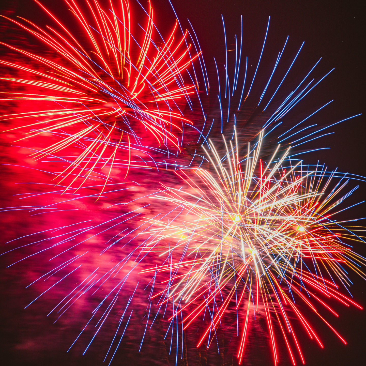 Colorful fireworks burst in the night sky, displaying red, blue, and yellow streaks.