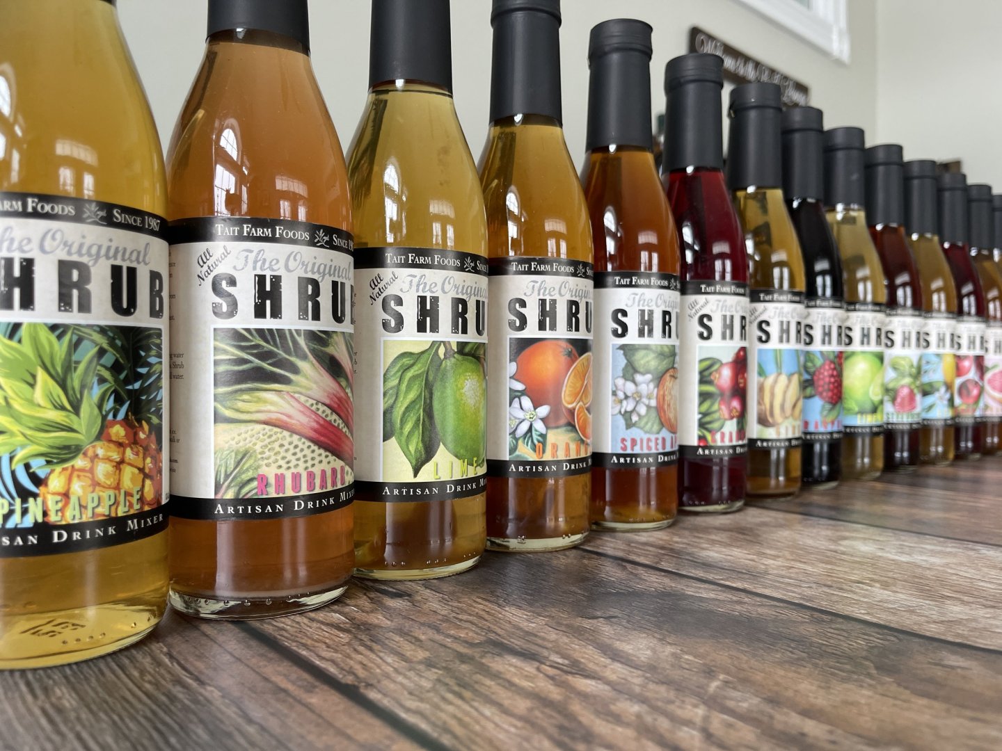 A row of colorful shrub syrup bottles on a wooden table.