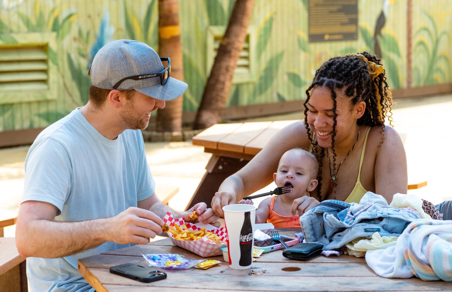 Family with a baby enjoying a meal at an outdoor picnic table.