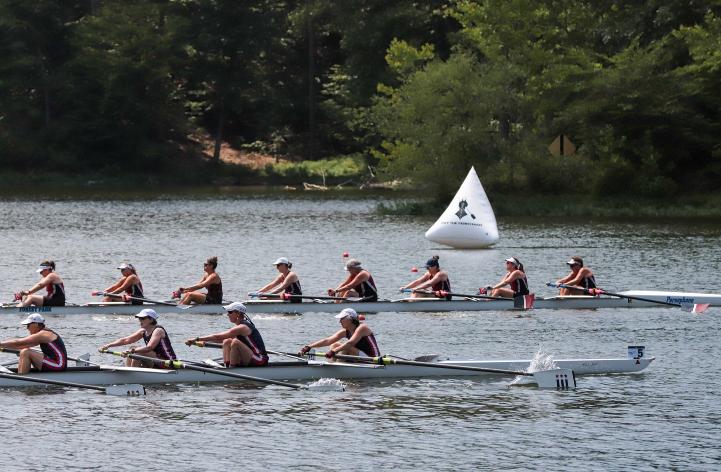 Rowers competing on a river, passing a buoy, surrounded by trees.