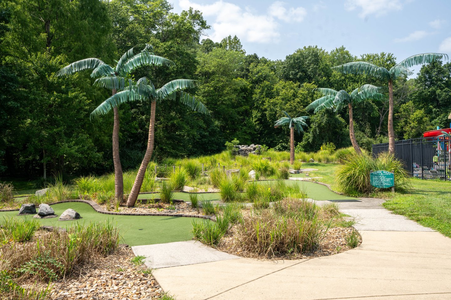 Mini-golf course with palm trees, green pathways, and lush greenery.