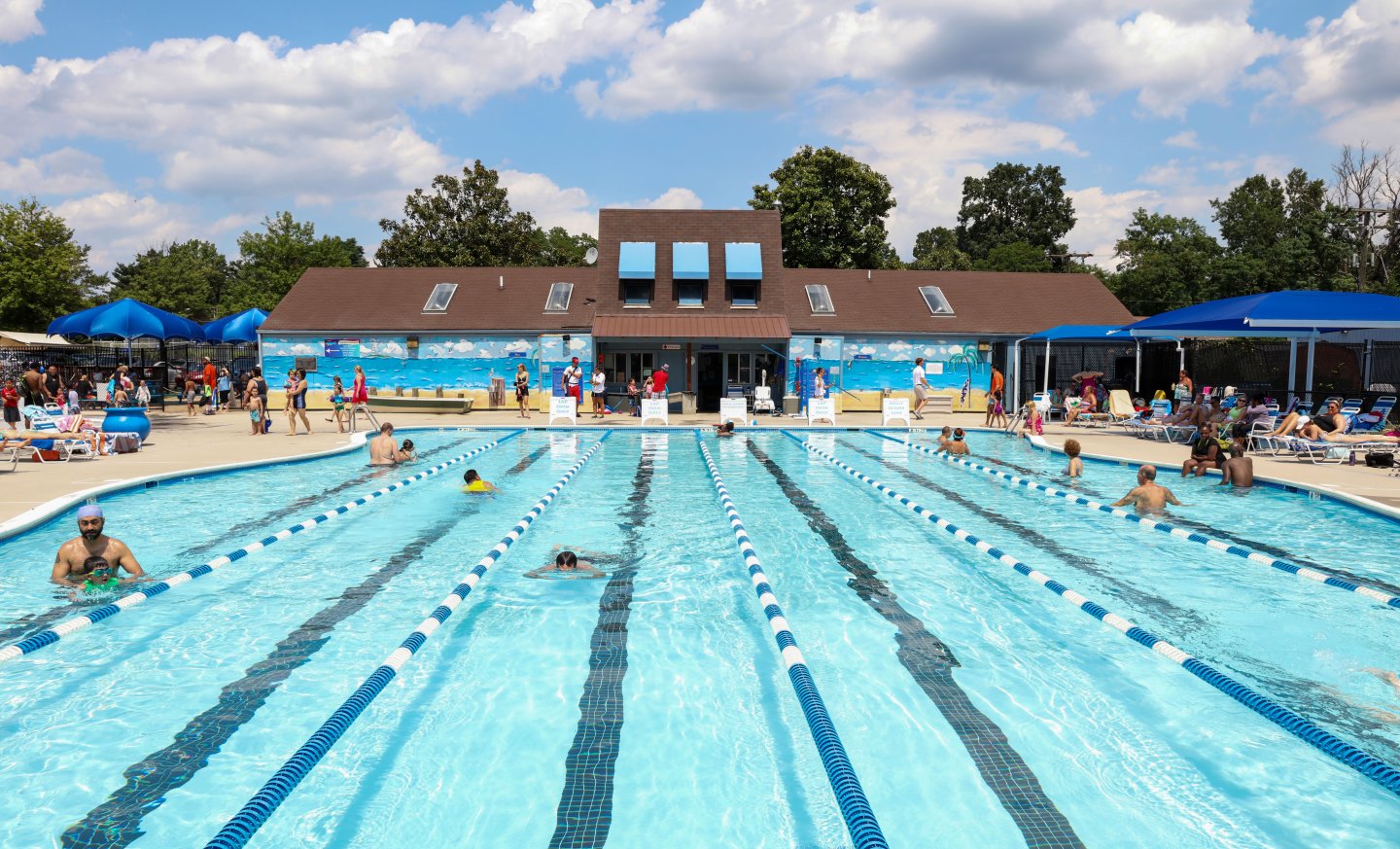 Outdoor swimming pool with people and a building in the background.