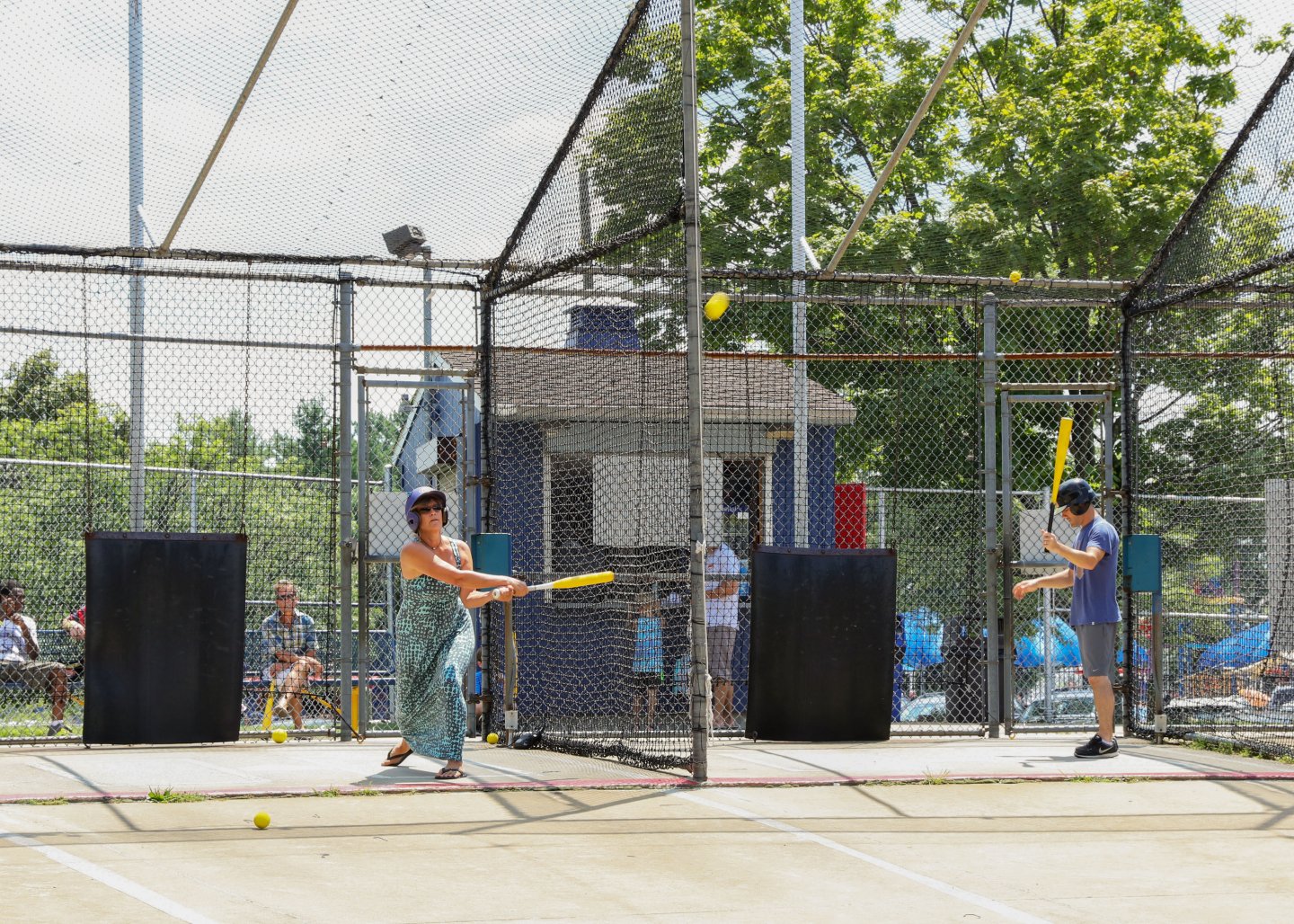 Batting cage with two people swinging yellow bats.