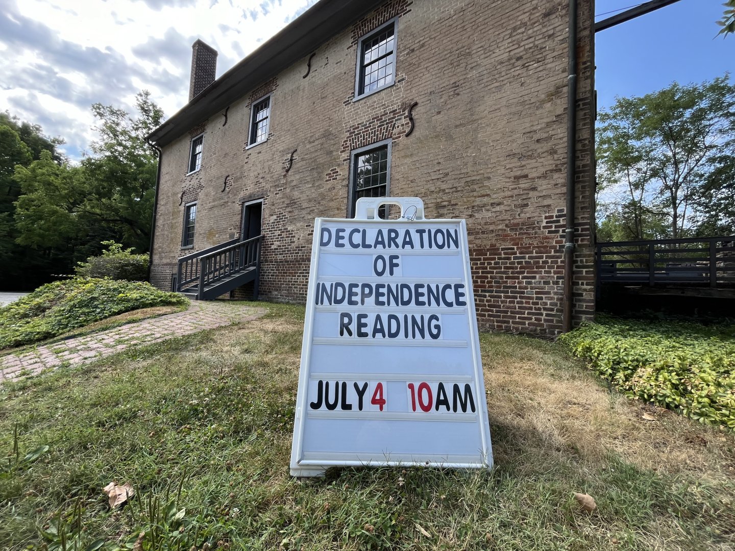 Sign announcing a July 4 event at a historic brick building.