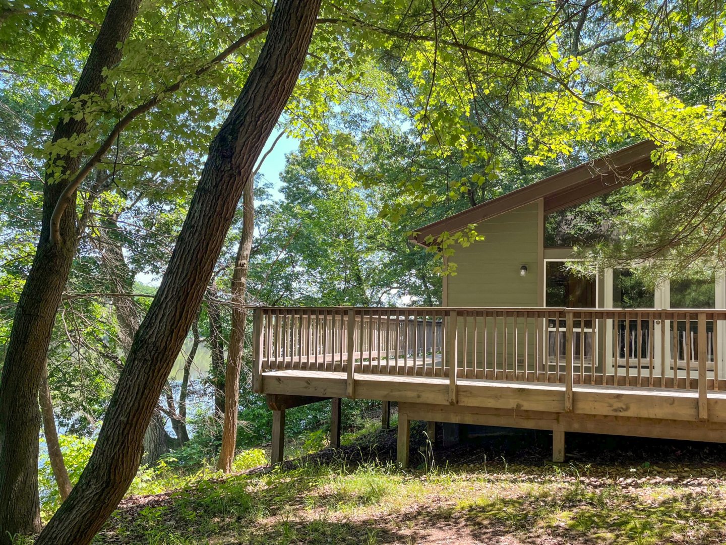 Cabin with wooden deck surrounded by lush trees and sunlight.