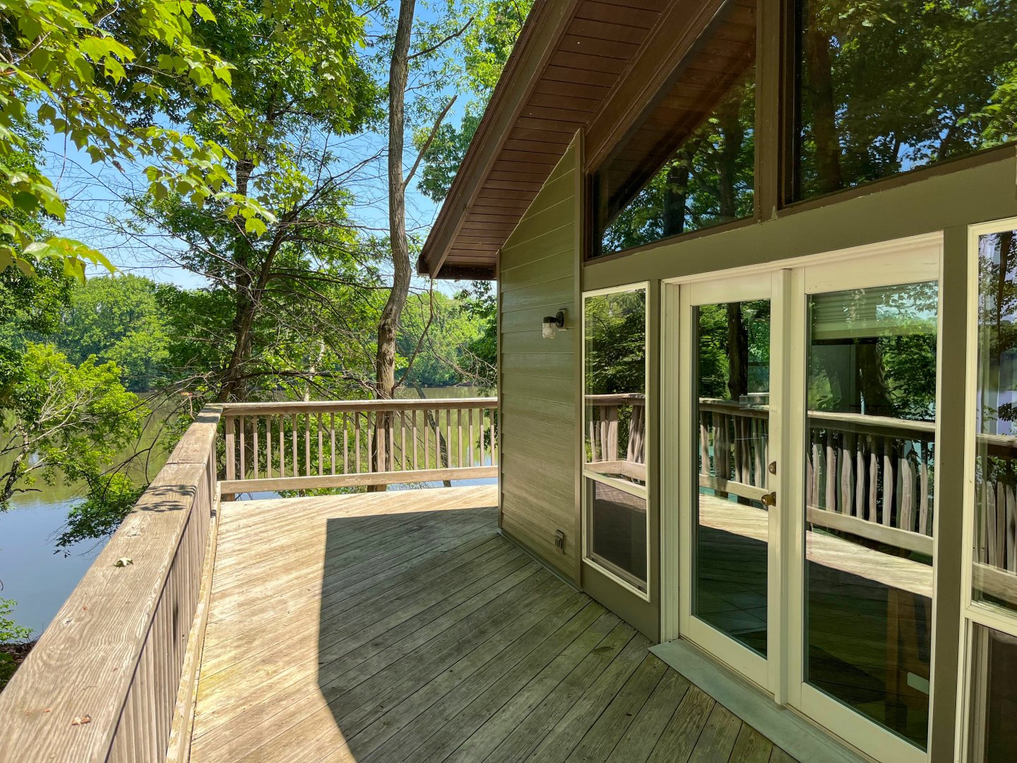 Wooden deck with glass doors overlooking lush trees and a river.