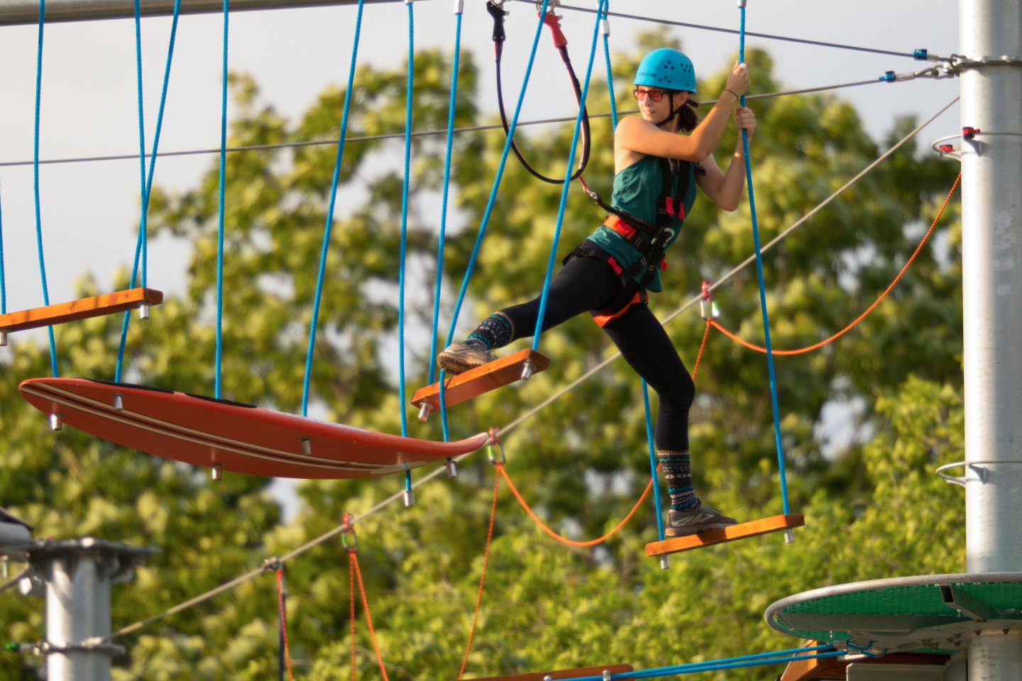 Person climbing an outdoor ropes course, wearing a helmet and harness.
