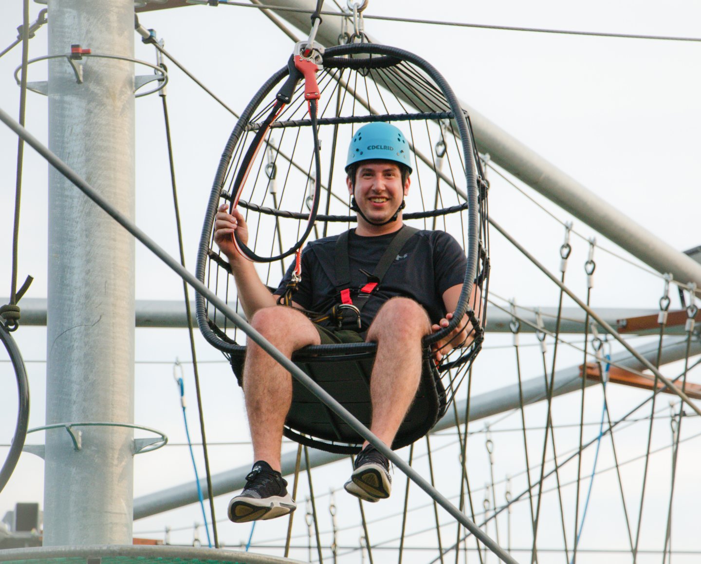 Man in a safety harness on a high ropes course, wearing a blue helmet.
