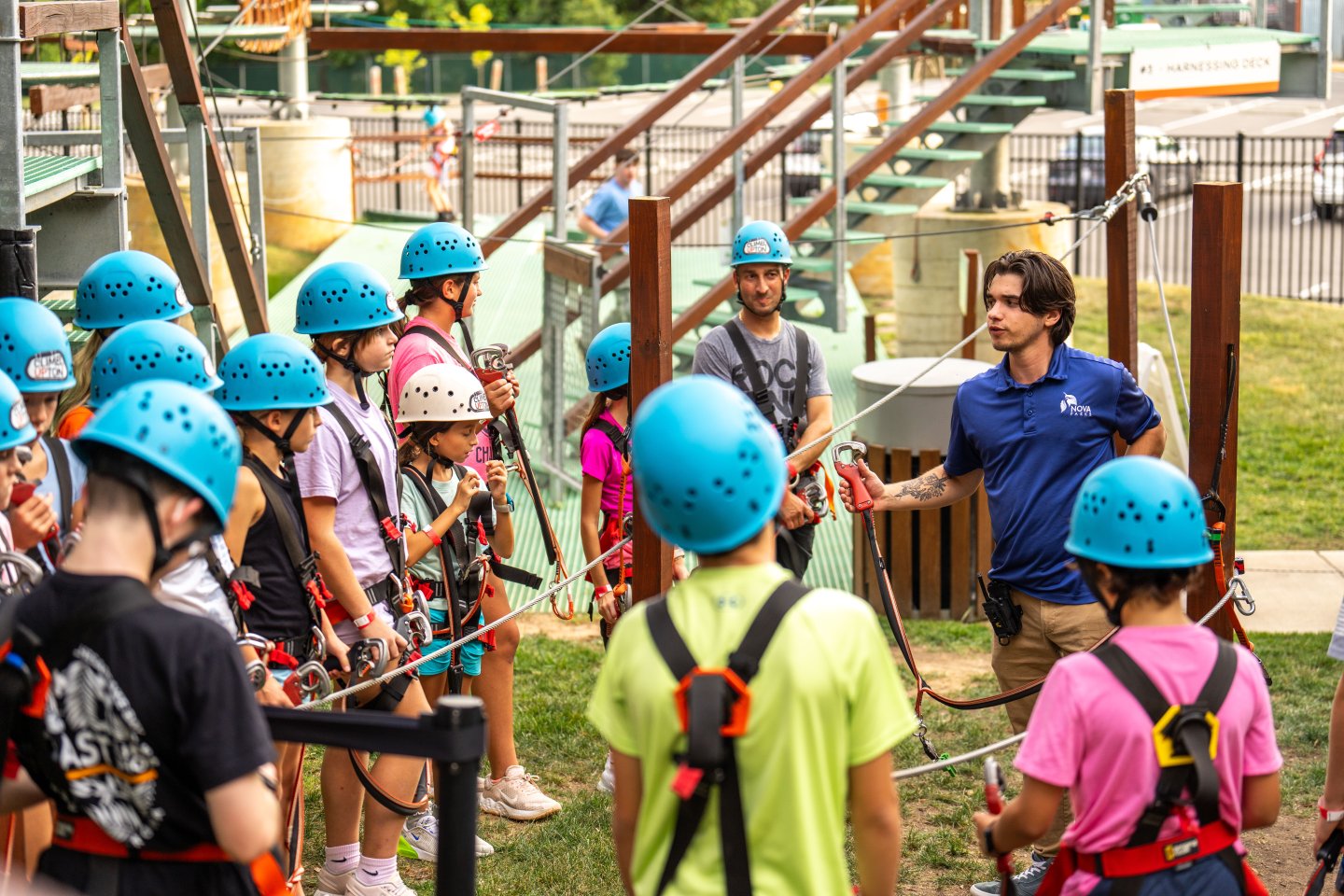 Group of kids in helmets listening to an instructor at a ropes course adventure park.