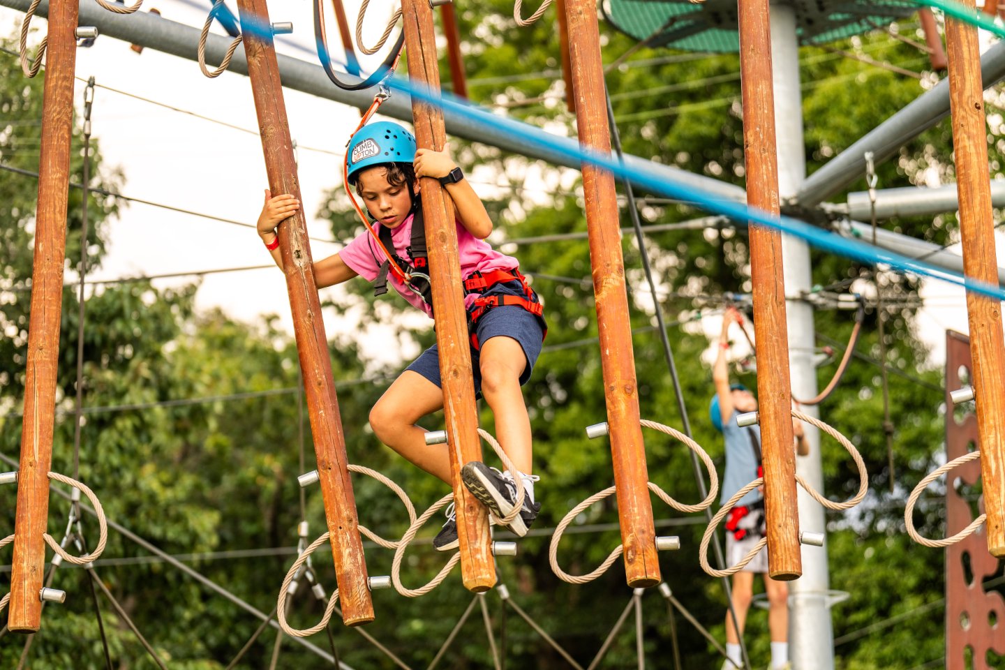 Child in helmet navigating a ropes course outdoors.