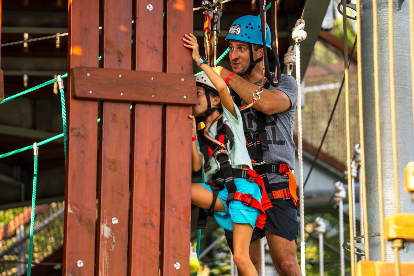 Man and child in helmets, standing by a wooden climbing element.