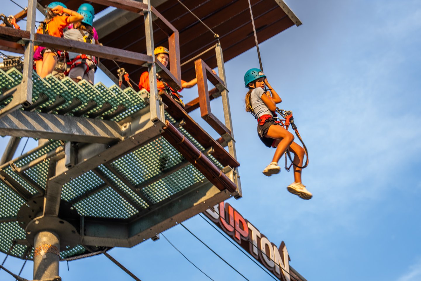 People ziplining from a platform under a clear blue sky.