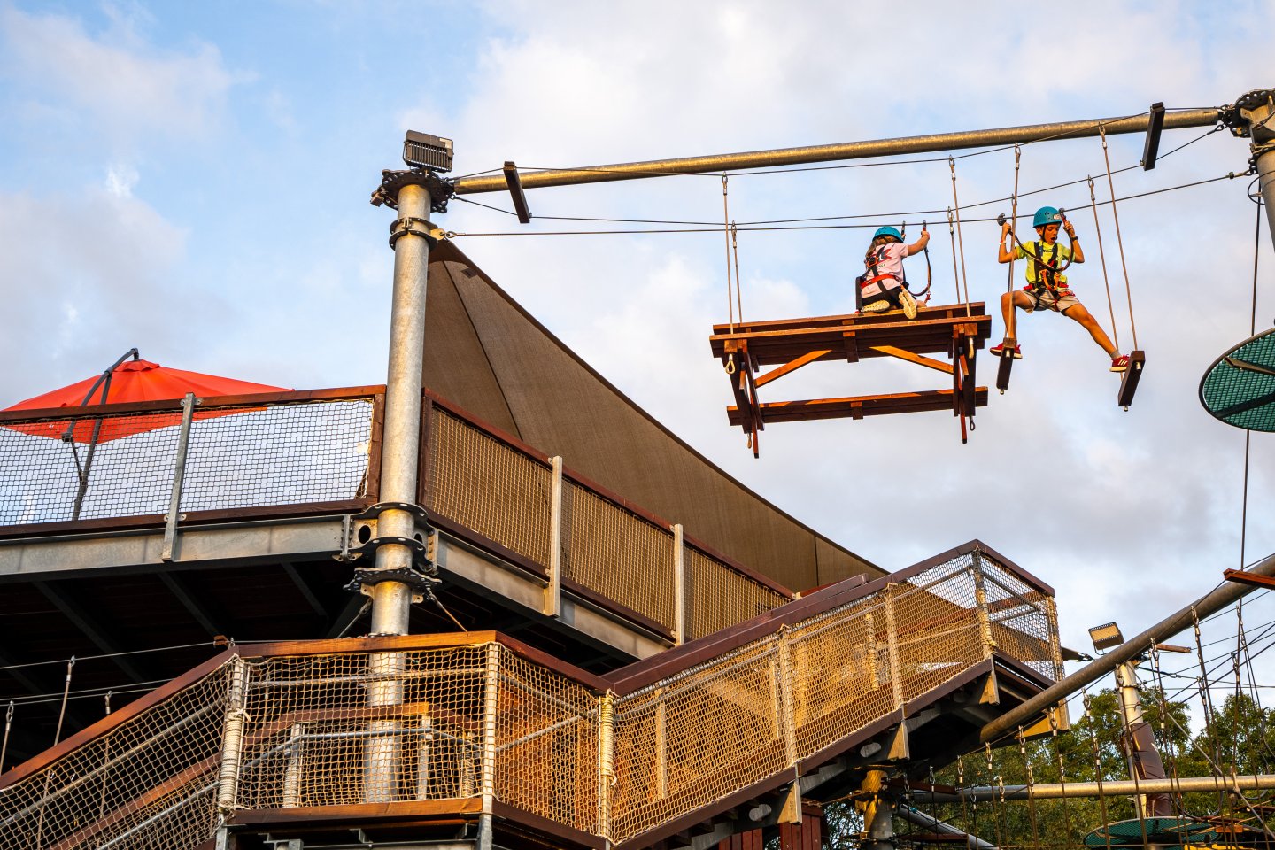 Two people on a high ropes course, under a cloudy sky.