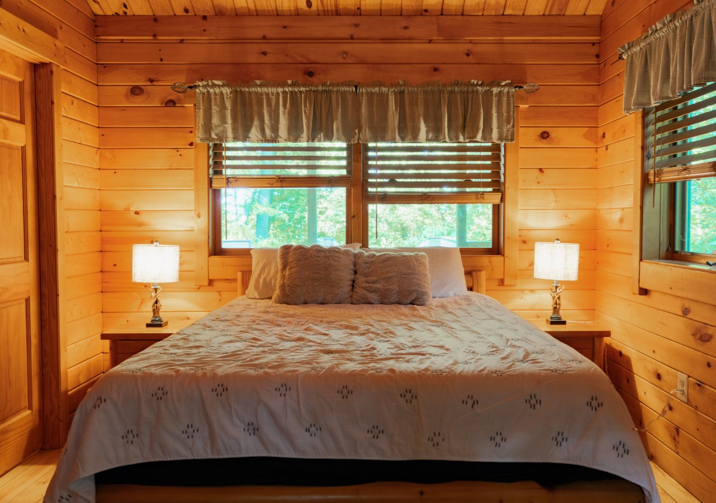 Cozy wooden bedroom with a double bed, lamps, and window with trees outside.