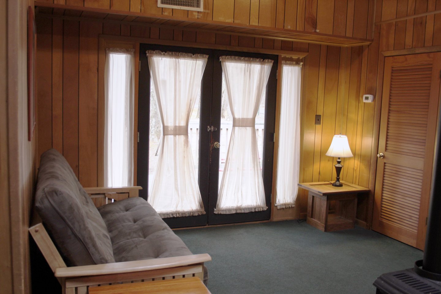 Cozy wooden room with a futon, lamp, and curtained glass doors.