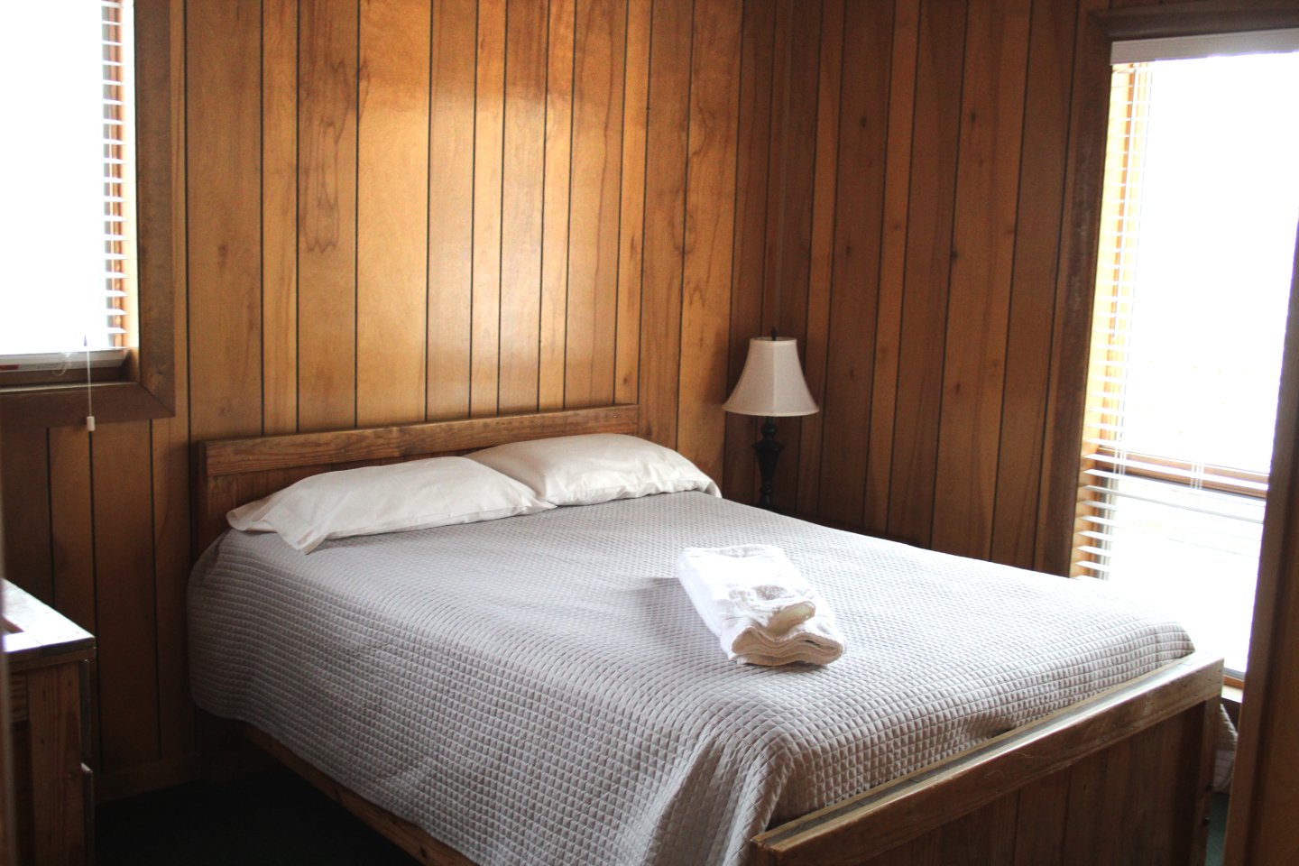Cozy wood-paneled bedroom with a double bed and a lamp.