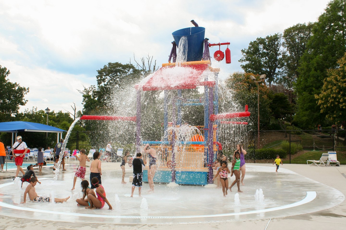 Children playing at a colorful water park splash pad under a large fountain.