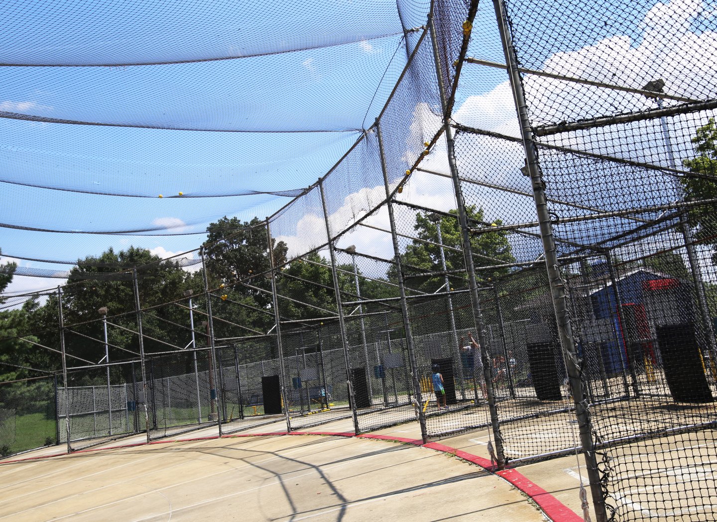 Batting cage under a blue sky with trees in the background.