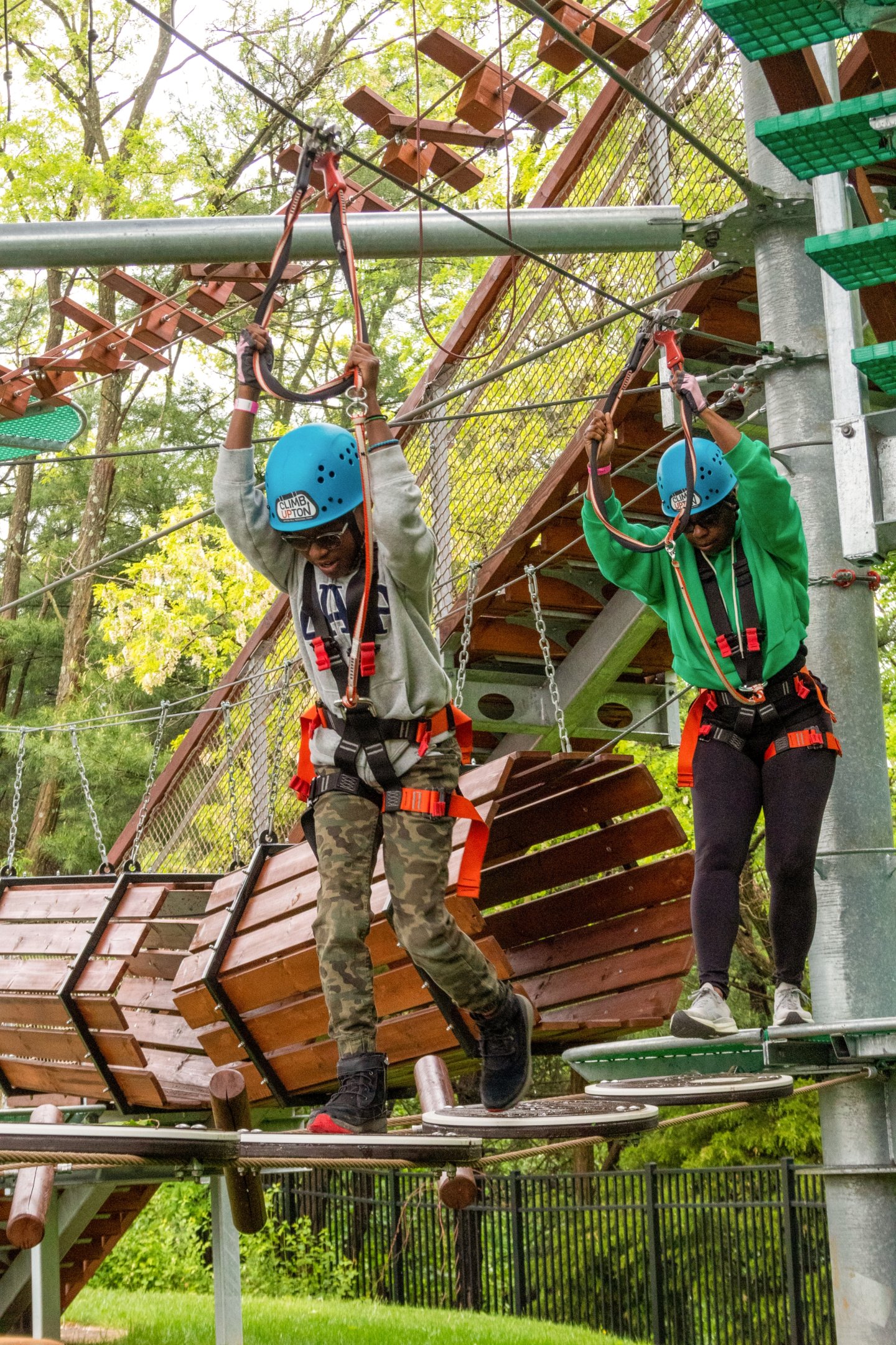 Two people in helmets navigate a ropes course outdoors.