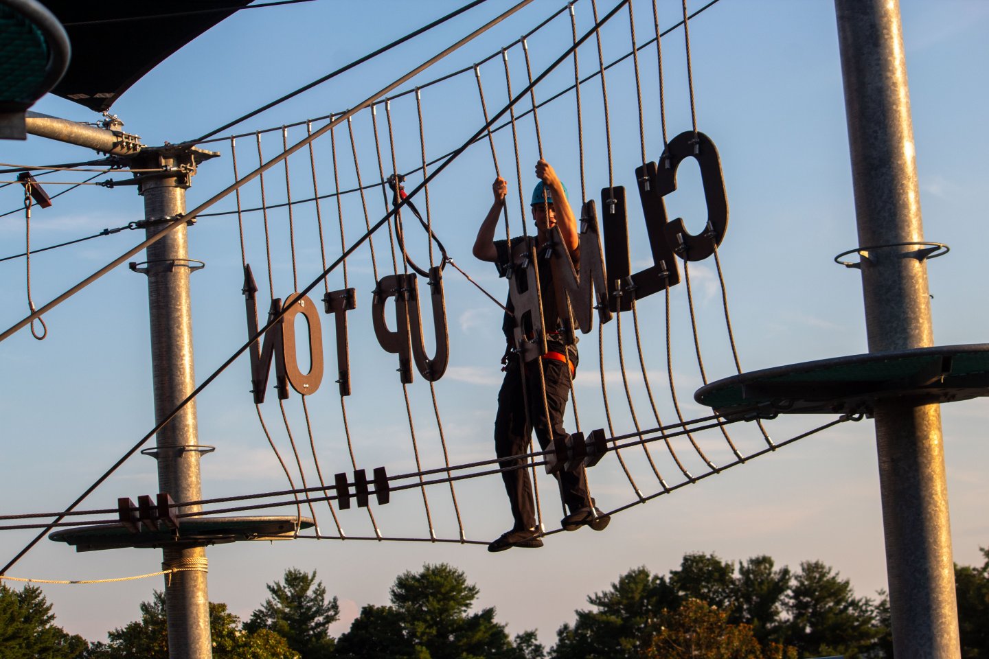 Person climbing a high rope course at sunset.