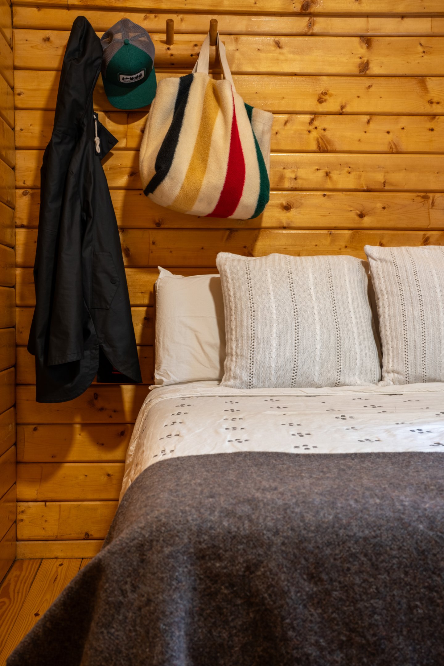 Cozy wooden room with a bed, coat, hat, and colorful bag hanging.