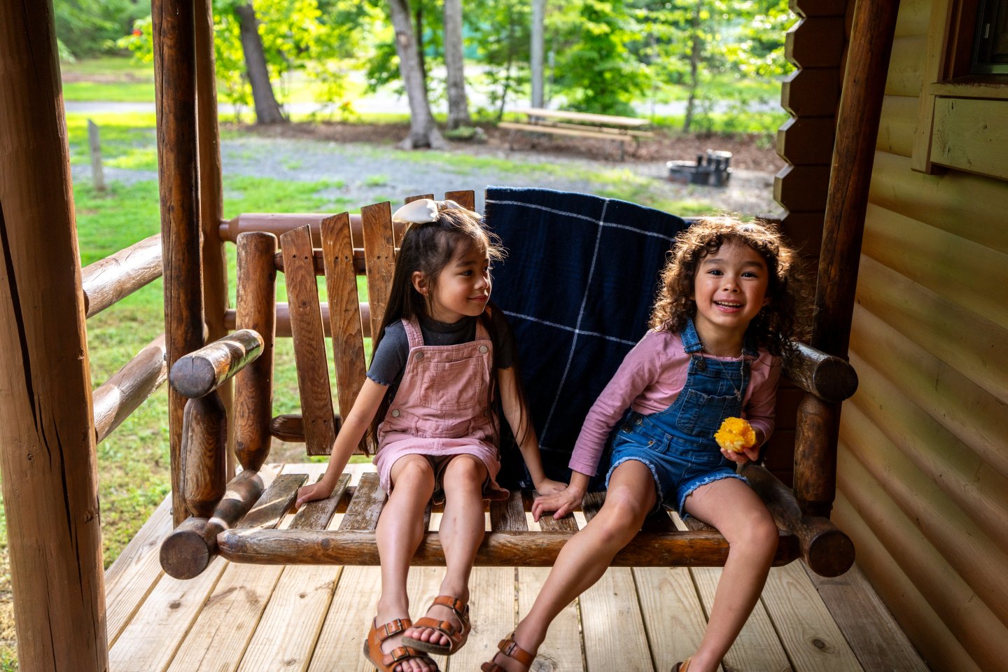 Two children laughing and sitting on a wooden porch swing.