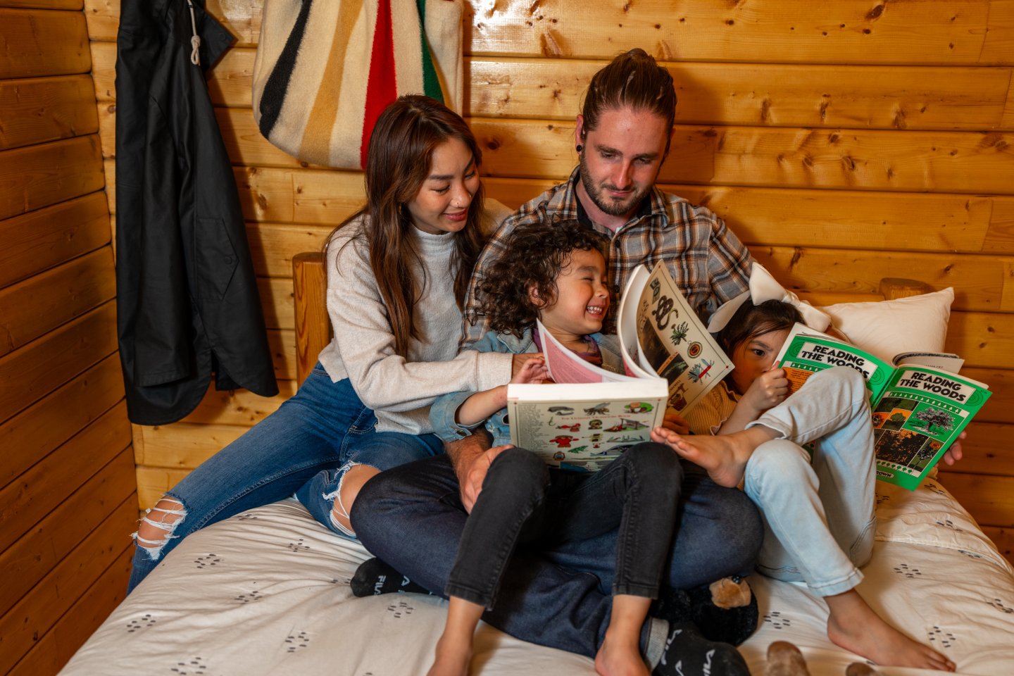 Family sitting on bed reading books together, wood-paneled room.