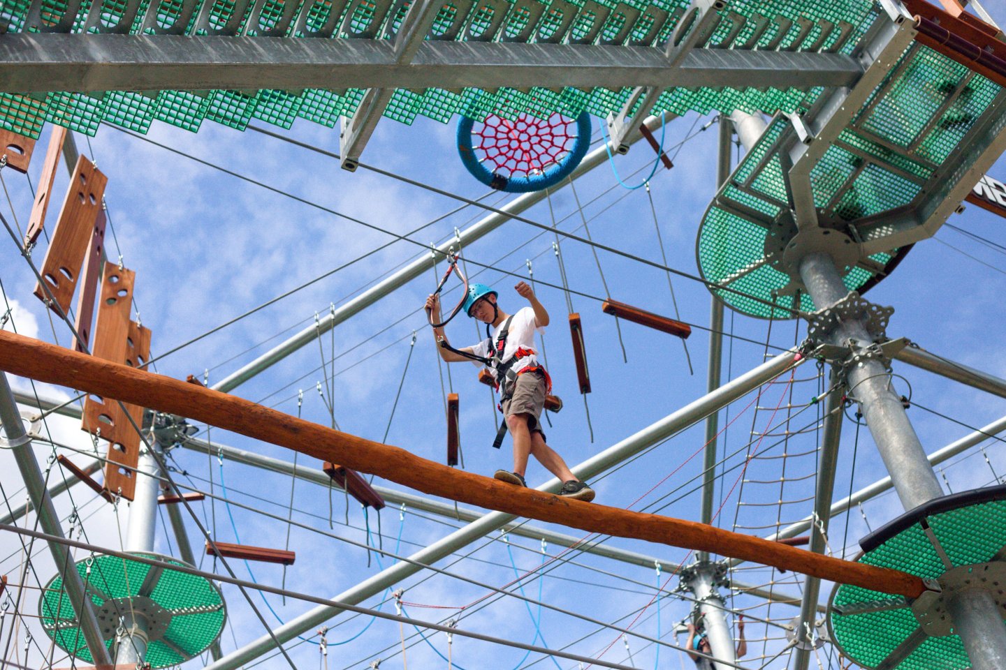 Rope course with person balancing on beam under a blue sky.