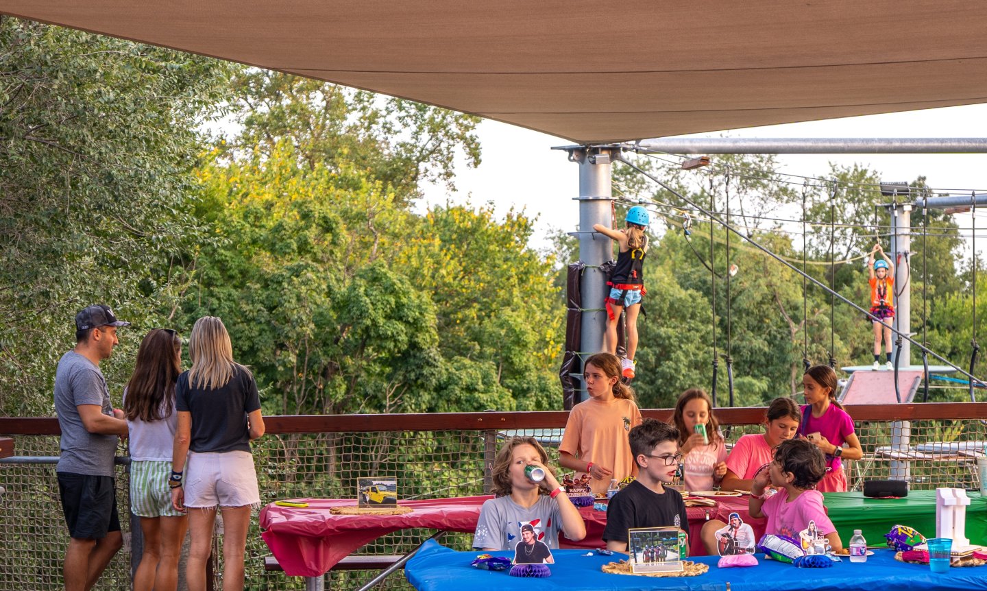Kids eating at picnic tables, others climbing a ropes course outdoors.