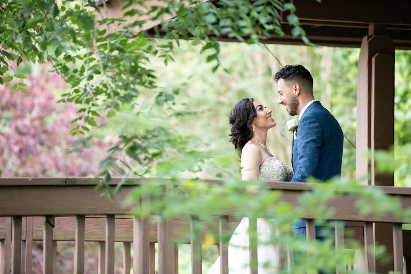 Bride and groom smiling under a gazebo surrounded by greenery.