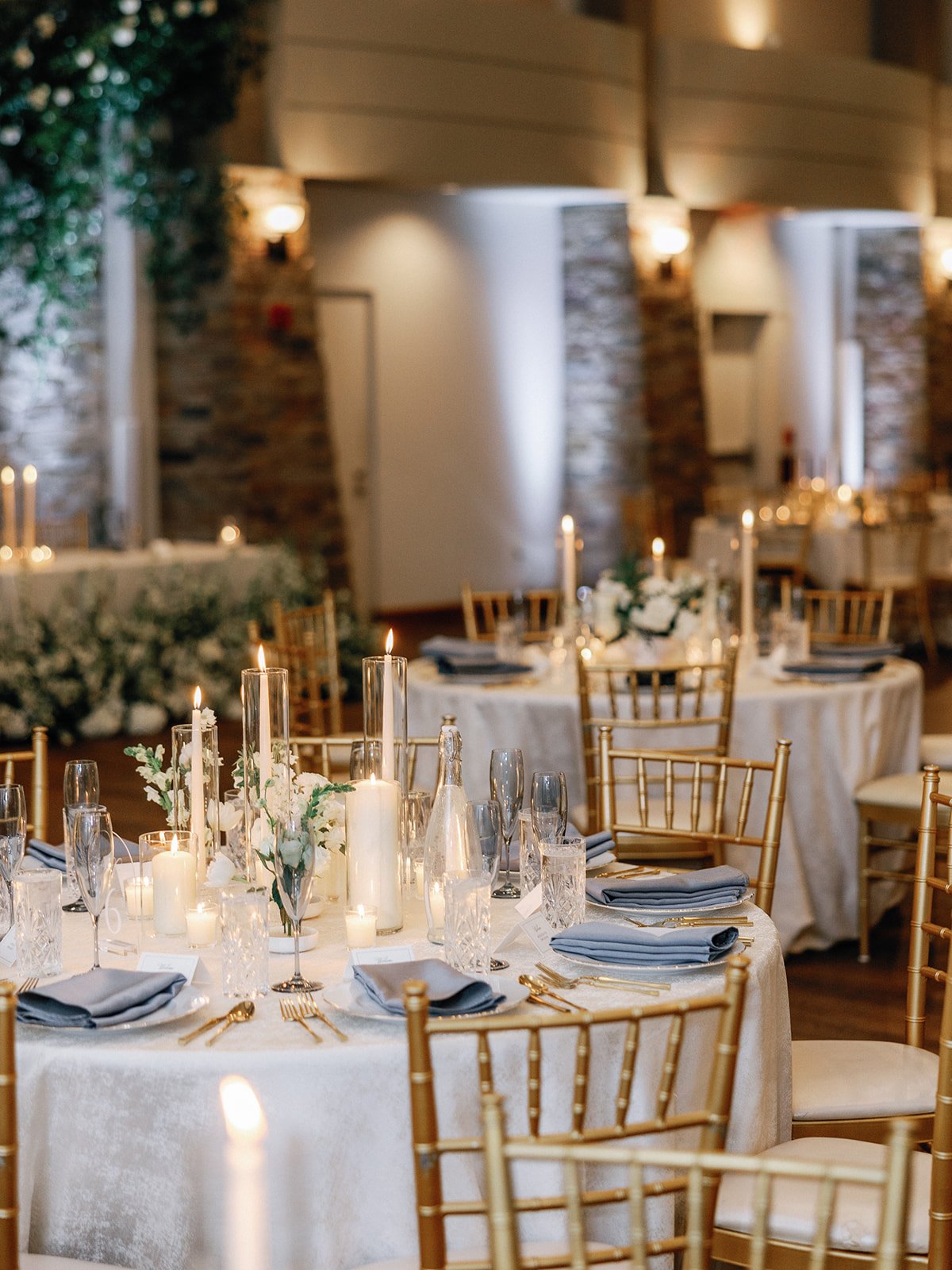 Elegant wedding tablescape with candles, gold chairs, and white tablecloths.