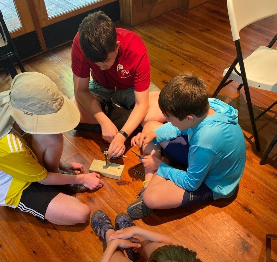 Three children and an adult engaged in an indoor activity on a wooden floor.