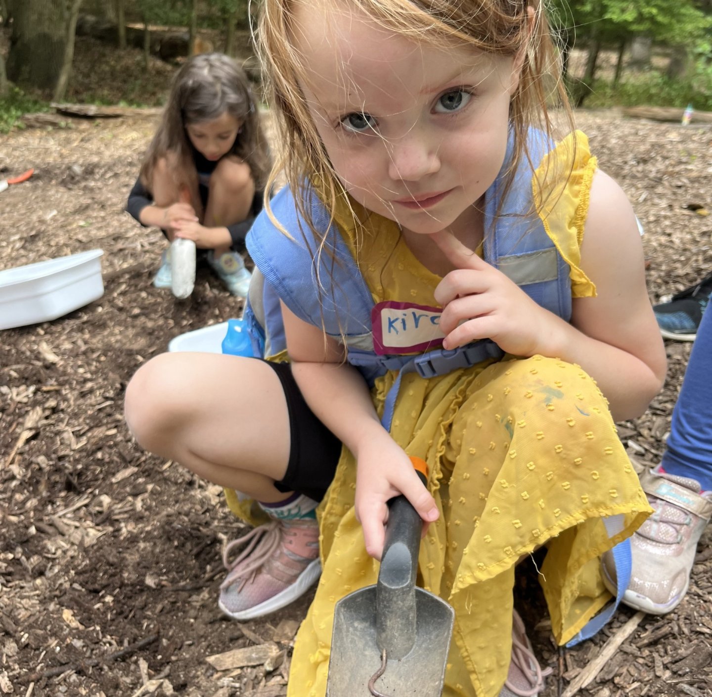 Child holding a trowel with a worm, outdoor setting, focused expression.